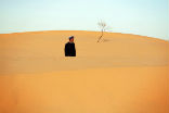 Image of A Chinese man gazes over the sand of an advancing dune. 