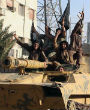 Image of Members of the Islamic State ride a captured tank through an Iraqi city displaying their black flags.