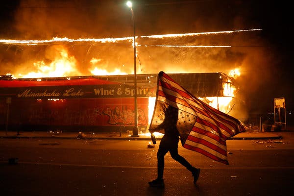 Image of A protester carries the American flag upside down, a symbol of distress as Minneapolis burns. 