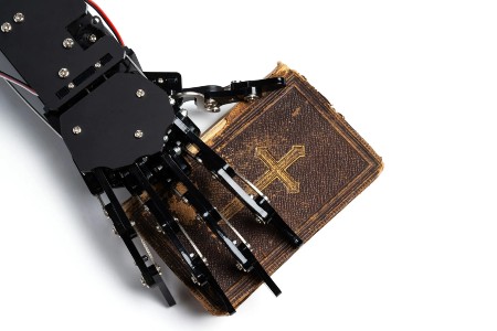 Image of Real AI robot's hand with the ancient Bible.