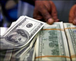 Image of A money changer displays stacks of 100 US dollar bills at a foreign exchange counter.