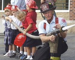 Image of KINDERGARTENERS GET HANDS-ON DEMONSTRATION – Four-year-old kindergarten students from Blessed Sacrament School get a hands-on demonstration of a water hose from firefighter Richard Vanwieringen, right, and Lt. Thomas Kizewski of the Milwaukee Fire Department Sept. 15. Fire department representatives visited the school after kindergarten students reported a house fire across the street from the school's playground during recess Sept. 13. (Catholic Herald)