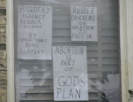 Image of You will see the intentional placement of a rubber chicken over the Corpus of Jesus Christ which is hung on the Cross. This is publicly displayed in the windows of this facility. This and other displays like it are absolute acts of blasphemy against God. They are also hate speech directed against Christians.