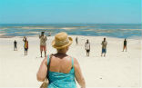 Image of A still from the film depicting a woman shopping for a male prostitute on the beach.