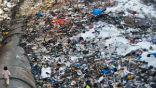 Image of A child walks barefoot atop a water pipe surrounded by a trash-filled cesspool. 