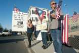Image of Protesters carry signs threatening to dig up Tsarnaev's grave. 