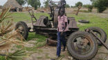 Image of A child plays around an abandoned anti-aircraft gun parked in a fallow field.