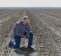 Image of A farmer surveys his field, left barren by drought, partly natural, partly man-made. 